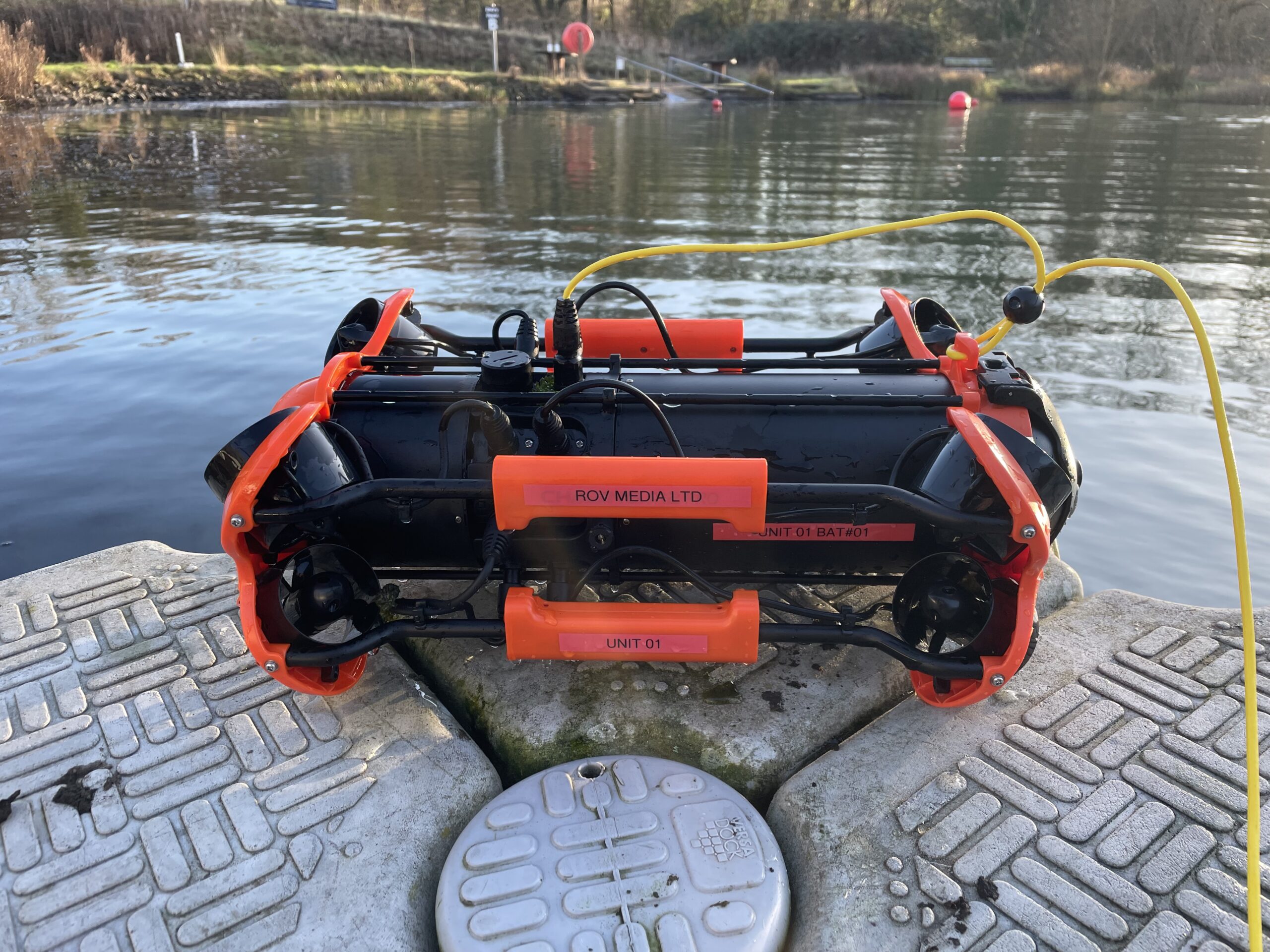 ROV Media CHASING M2 Pro underwater ROV with orange protective frame and yellow tether at the water's edge.