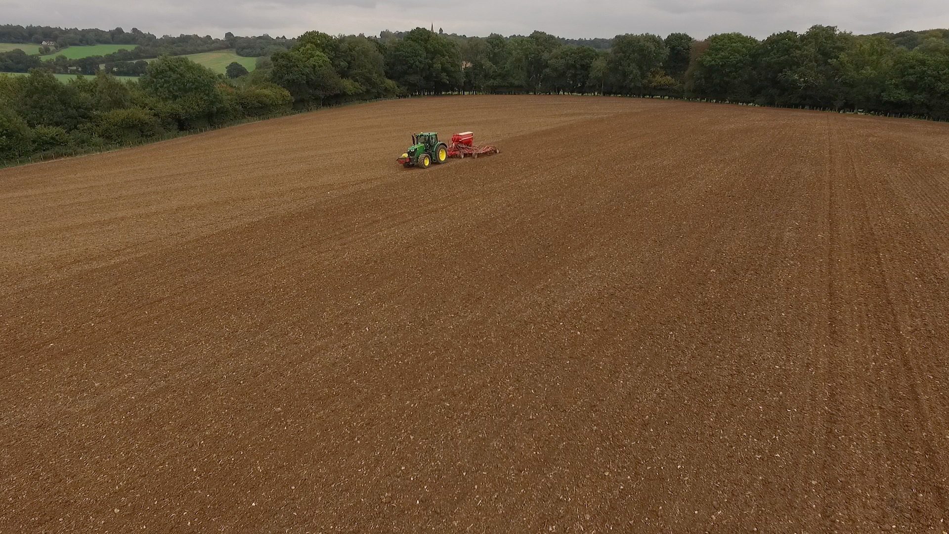 Aerial view of a tractor working across a cultivated field beside a tree line