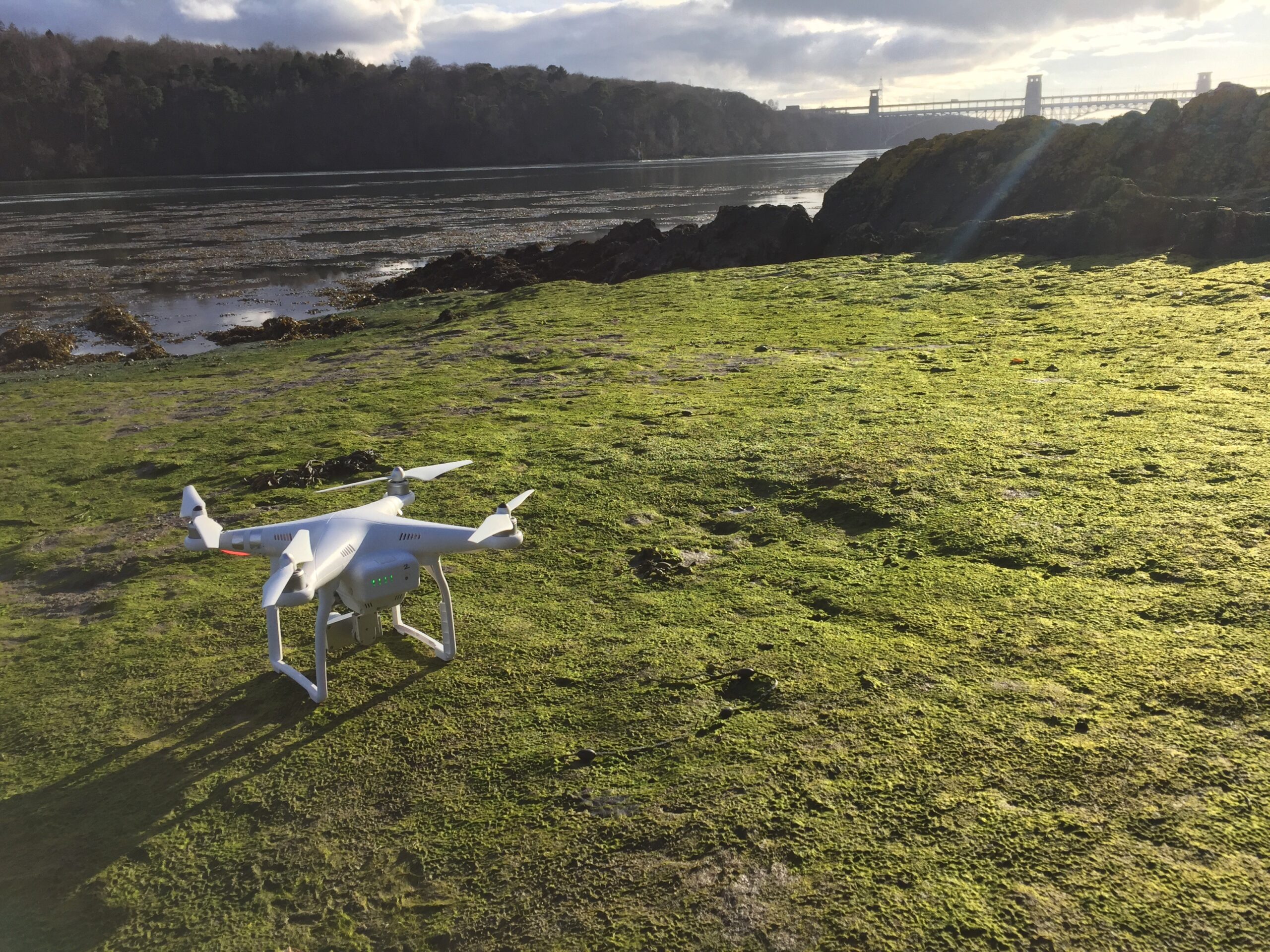 Aerial drone prepared on coastal grass beside a tidal estuary